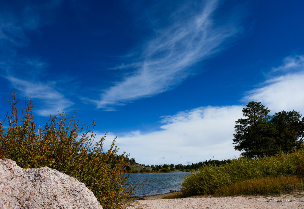 Entrance to Trailhead overlooking the lake surrounded by rock outcroppings, grass, trees and shrubs at West Lake State Park in Red Feather Lakes, Colorado
