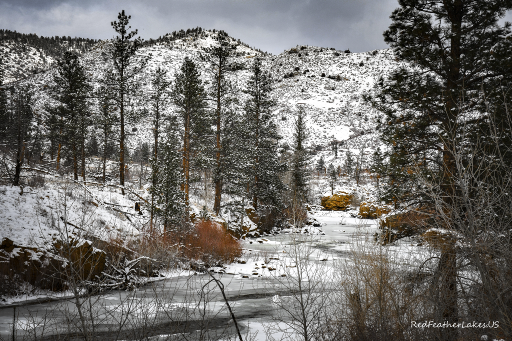 A snowy scene of the Poudre River against a backdrop of the Rocky Mountains.