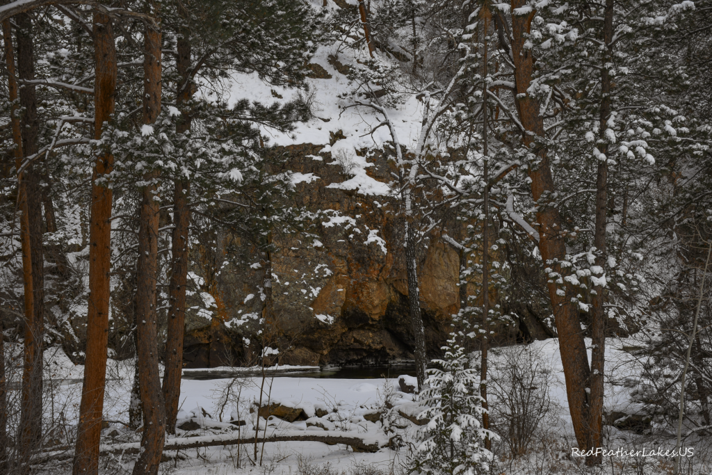 A Large Cliff Overhangs the Cache La Poudre River in a Dark & Quiet Winter Scene