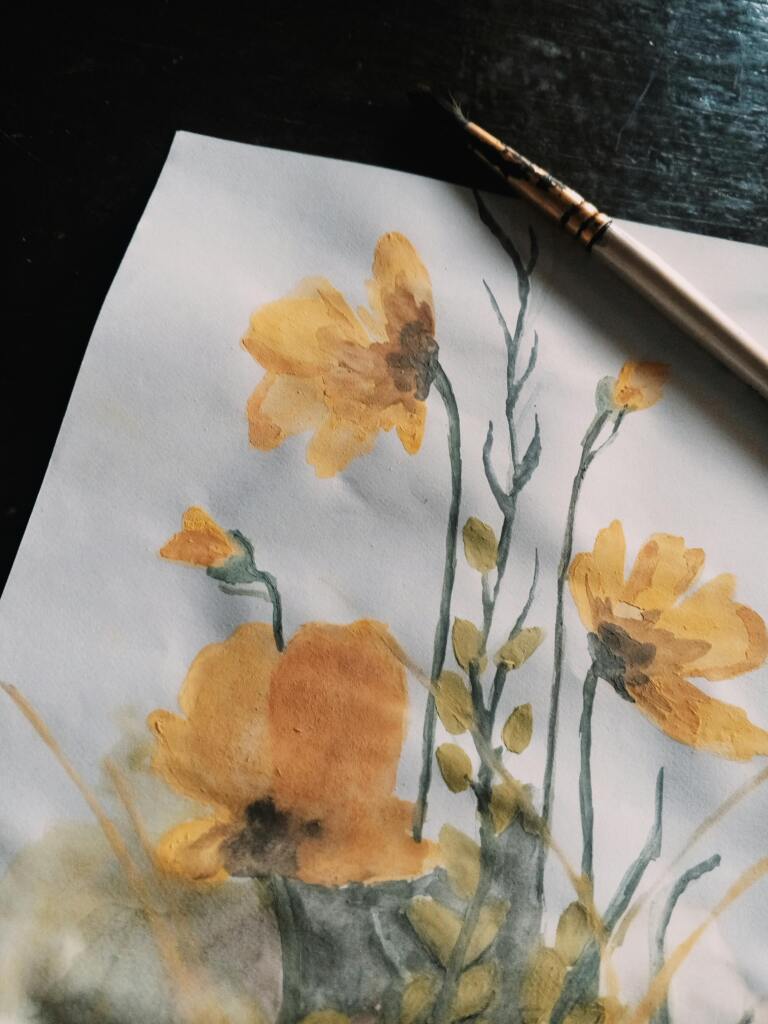 A close-up of a yellow floral watercolor painting with a paintbrush on dark surface.
