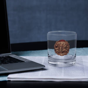 Glass with Red Feather logo beside laptop
