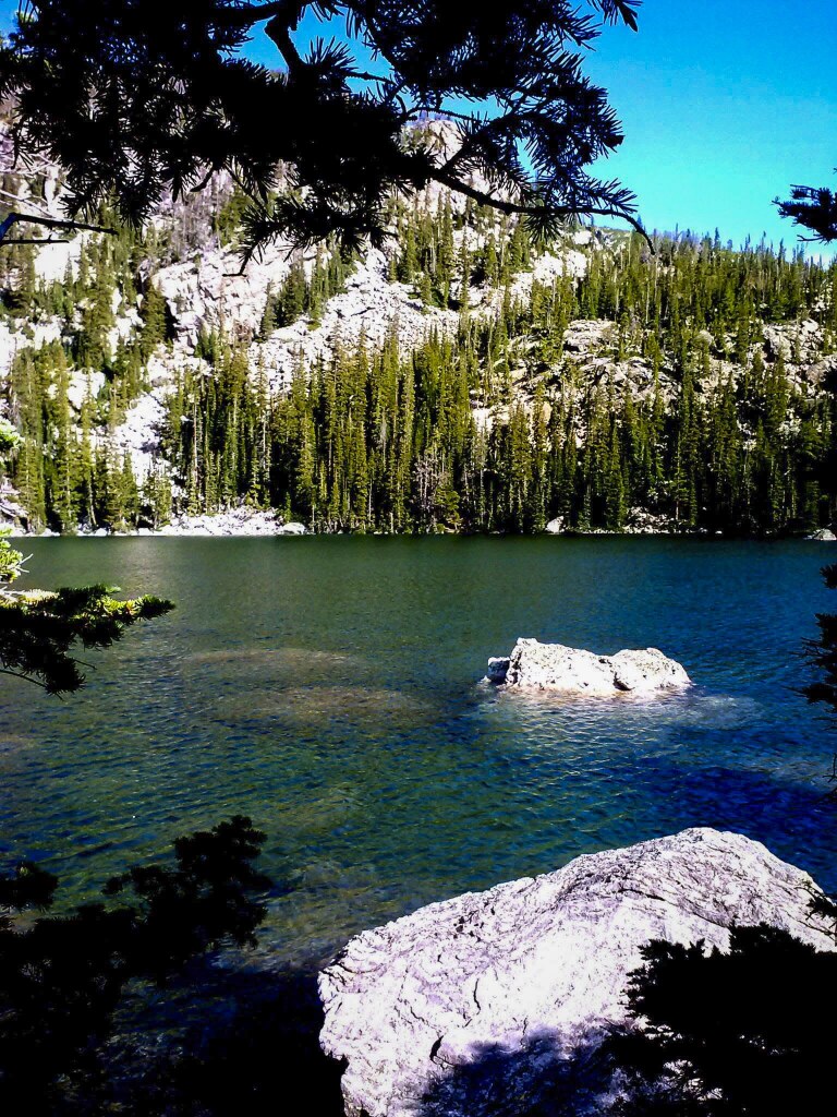 Pale granite boulders standing out of the clear blue-green water of Lake Haiyaha below a forested granite slope, Rocky Mountain National Park