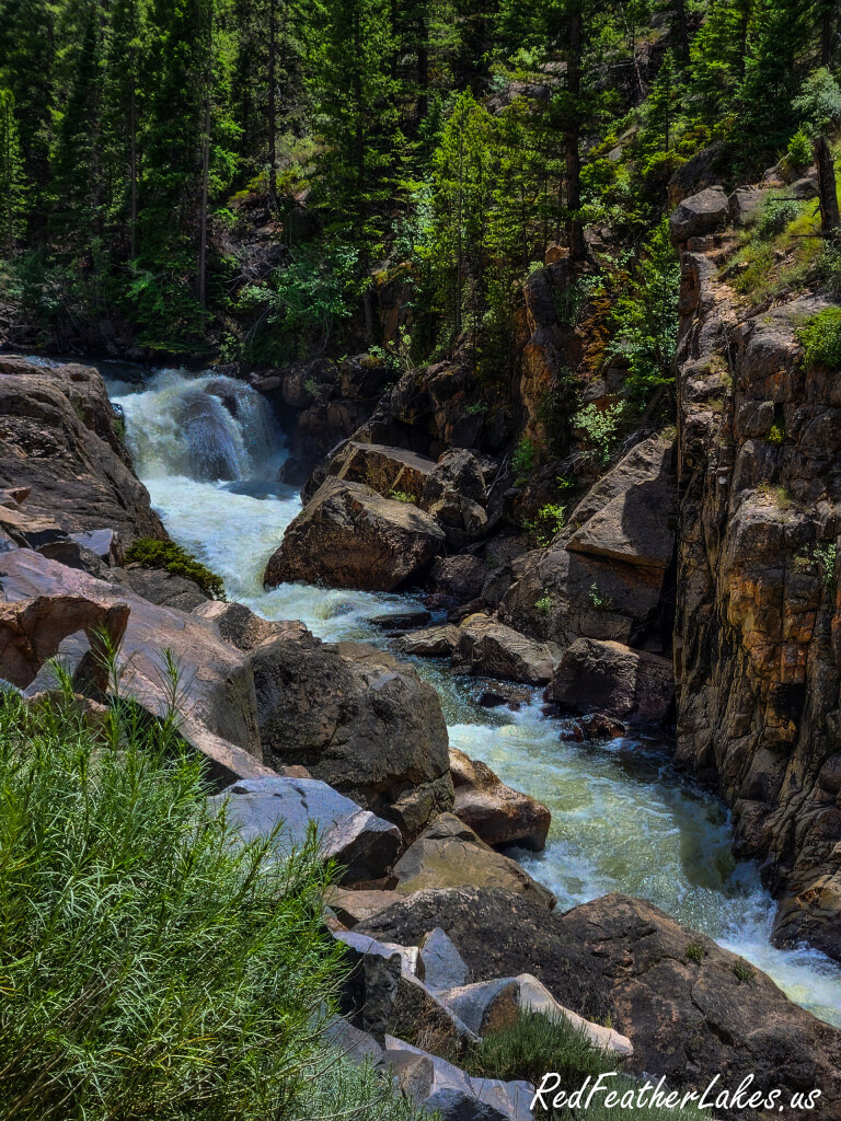 A waterfall tumbling over rock amid pines beside the Cache la Poudre River on the Cache la Poudre Scenic Byway in Poudre Canyon, Colorado