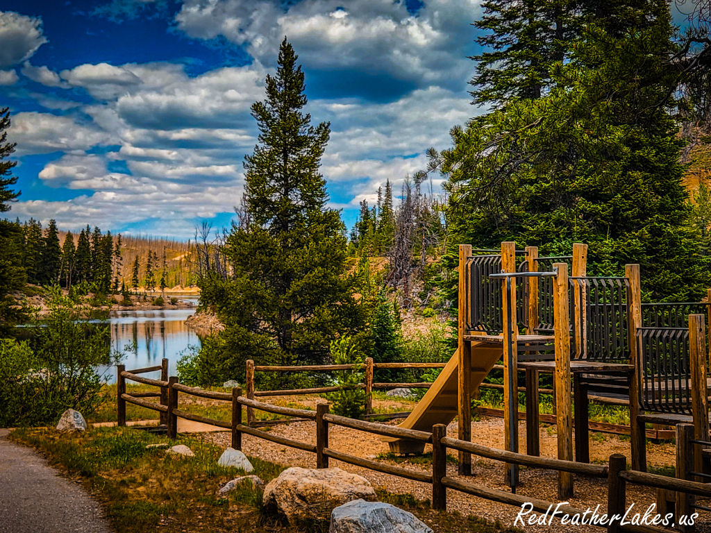 Chambers Lake and its day-use area with a children's playground and split-rail fence beneath a dramatic Colorado sky