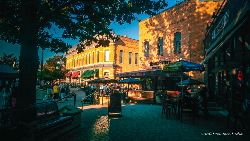 Historic Old Town Square in downtown Fort Collins, Colorado at golden hour, with brick storefronts, sidewalk café umbrellas and CooperSmith's Pub & Brewing