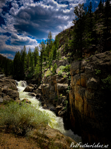 Poudre Falls tumbling through a granite gorge under towering clouds along Highway 14 in the Upper Poudre Canyon